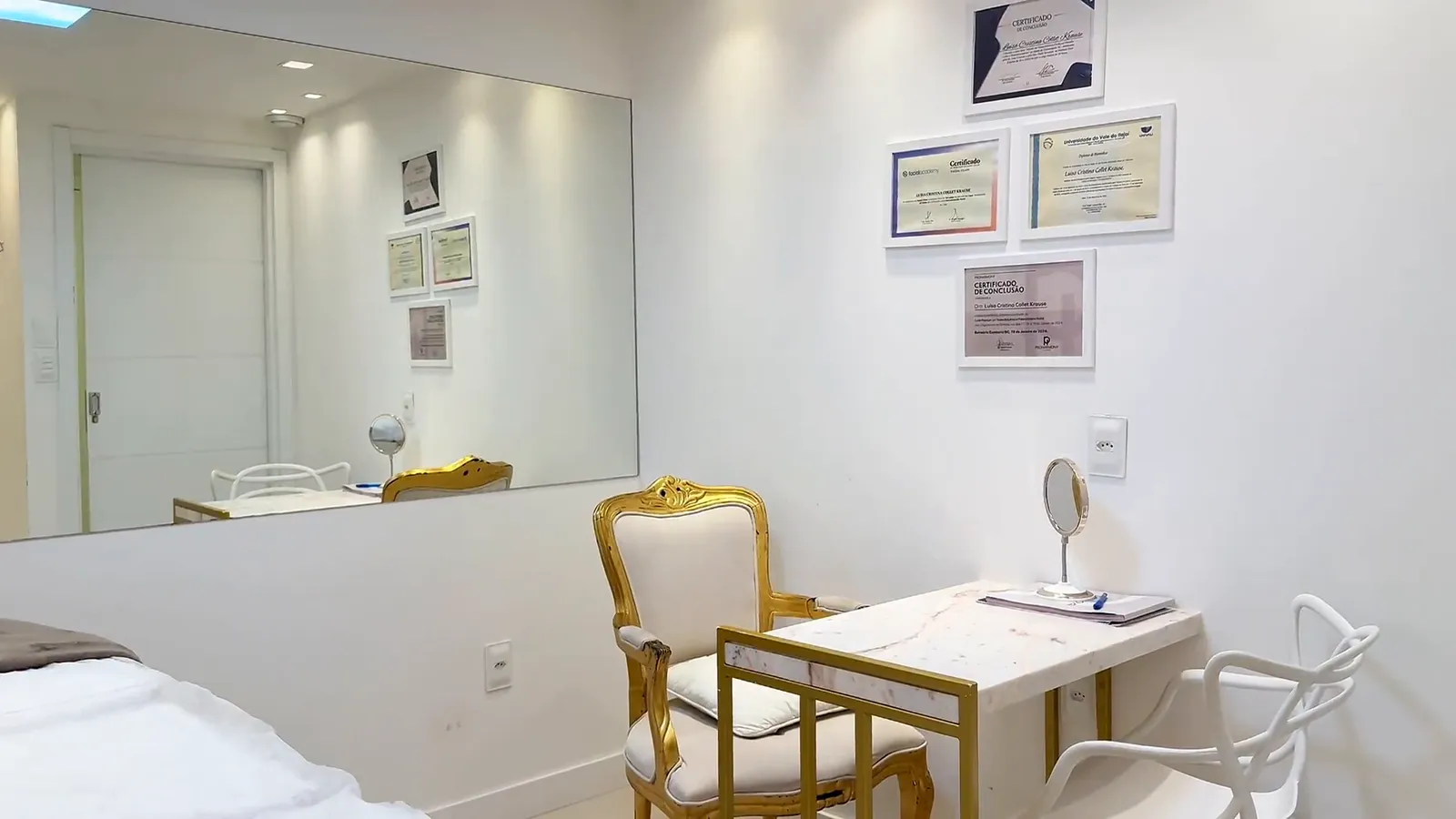Mesa de atendimento com cadeira dourada, espelho de mesa e certificados na parede